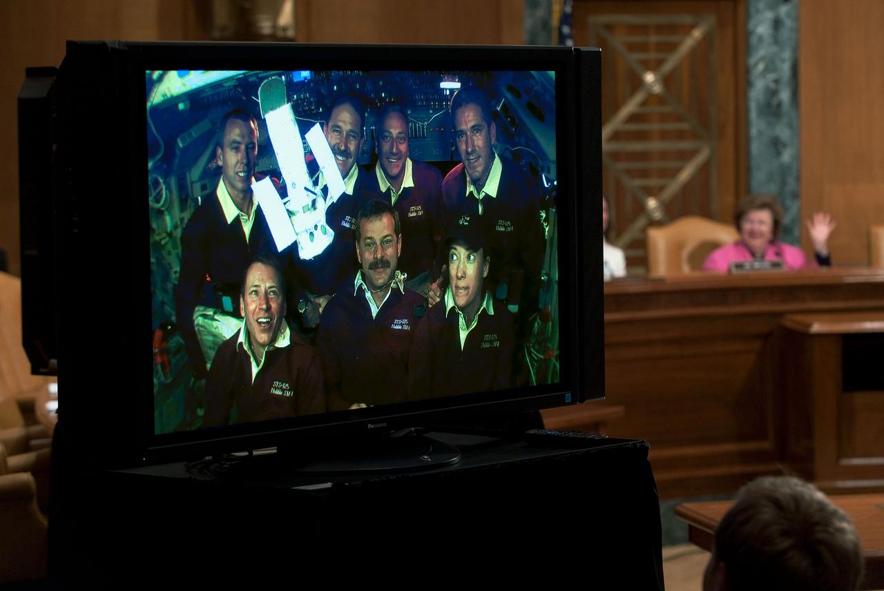 JSC2009-E-121340 (21 May 2009) --- The astronaut crewmembers of the STS-125 flight orbiting Earth aboard the Space Shuttle Atlantis are seen on a TV screen as they receive a phone call from U.S. Senator Barbara Mikulski (D-Md.) the day after the crew released the freshly serviced Hubble Space Telescope. Photo credit: NASA/Paul Alers
