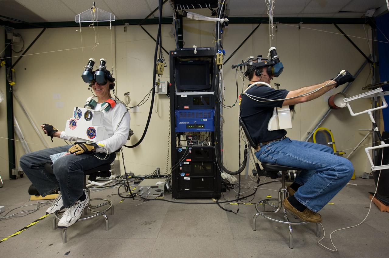 JSC2009-E-214341 (25 Sept. 2009) --- NASA astronauts Clayton Anderson (left) and Rick Mastracchio, both STS-131 mission specialists, use virtual reality hardware in the Space Vehicle Mock-up Facility at NASA's Johnson Space Center to rehearse some of their duties on the upcoming mission to the International Space Station. This type of virtual reality training allows the astronauts to wear a helmet and special gloves while looking at computer displays simulating actual movements around the various locations on the station hardware with which they will be working.