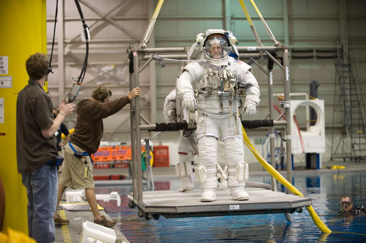 JSC2009-E-215170 (30 Sept. 2009) --- Astronauts Mike Good and Garrett Reisman (mostly obscured), both STS-132 mission specialists, attired in training versions of their Extravehicular Mobility Unit (EMU) spacesuit, are about to be submerged in the waters of the Neutral Buoyancy Laboratory (NBL) near NASA's Johnson Space Center. Divers are in the water to assist the crew members in their rehearsal, intended to help prepare them for work on the exterior of the International Space Station.
