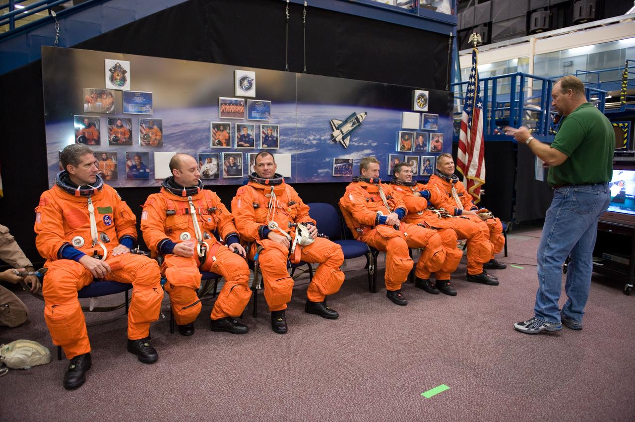 JSC2009-E-224123 (20 Oct. 2009) --- United Space Alliance crew trainer Robert H. (Rob) Tomaro (standing) briefs astronauts Mike Good (seated, left), Garrett Reisman, both STS-132 mission specialists; Tony Antonelli, pilot; Ken Ham, commander; Steve Bowen and Piers Sellers, both mission specialists, during a training session in the Space Vehicle Mock-up Facility at NASA?s Johnson Space Center. The crew members are attired in training versions of their shuttle launch and entry suits.