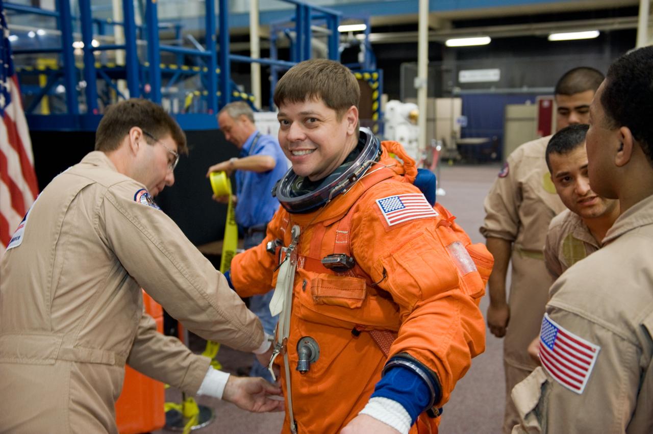 JSC2009-E-242832 (19 Nov. 2009) --- Astronaut Robert Behnken, STS-130 mission specialist, dons a training version of his shuttle launch and entry suit in preparation for a training session in the Space Vehicle Mockup Facility at NASA's Johnson Space Center. United Space Alliance suit technician Mike Thompson (left) assisted Behnken.