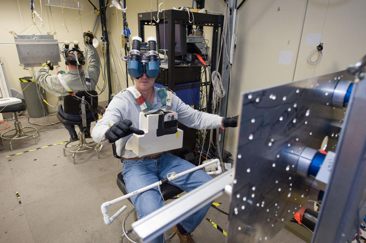 JSC2010-E-014962 (28 Jan. 2010) --- NASA astronauts Michael Good (foreground) and Garrett Reisman, both STS-132 mission specialists, use virtual reality hardware in the Space Vehicle Mock-up Facility at NASA's Johnson Space Center to rehearse some of their duties on the upcoming mission to the International Space Station. This type of virtual reality training allows the astronauts to wear a helmet and special gloves while looking at computer displays simulating actual movements around the various locations on the station hardware with which they will be working.