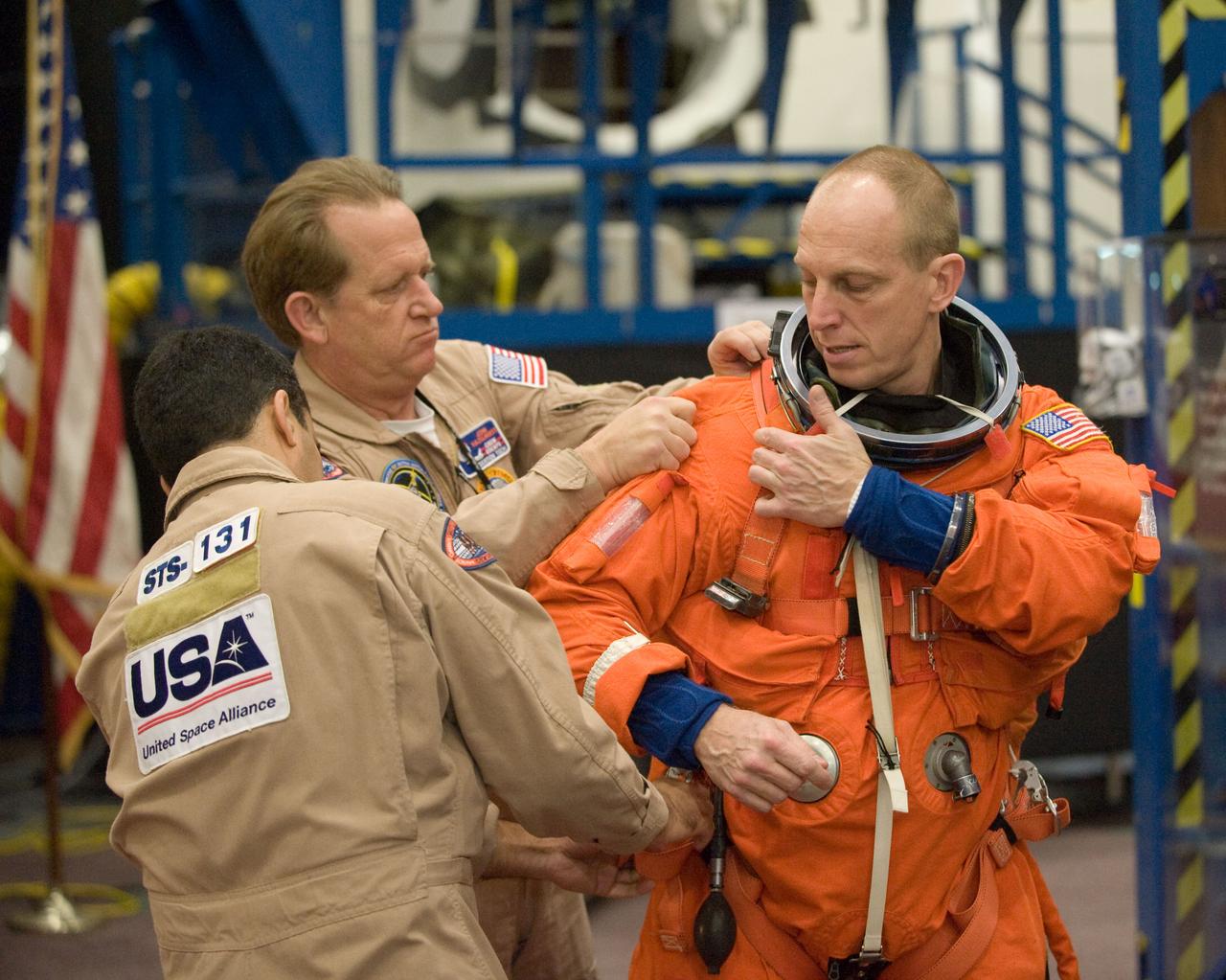 JSC2010-E-017726 (29 Jan. 2010) --- NASA astronaut Clay Anderson, STS-131 mission specialist, dons a training version of his shuttle launch and entry suit in preparation for an ingress/egress training session in the Space Vehicle Mock-up Facility at NASA's Johnson Space Center. United Space Alliance suit technicians Raymond Cuevas and John Hazelhurst assisted Anderson.