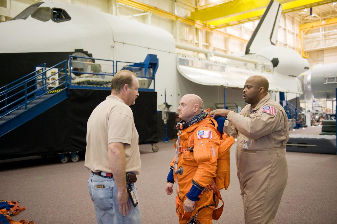 JSC2010-E-018579 (3 Feb. 2010) --- United Space Alliance (USA) crew trainer Robert (Rob) Tomaro (left) briefs NASA astronaut Mark Kelly, STS-134 commander, prior to the start of a training session in the Space Vehicle Mock-up Facility at NASA's Johnson Space Center. USA suit technician Andre Denard (right) assisted Kelly with the donning a training version of his shuttle launch and entry suit.