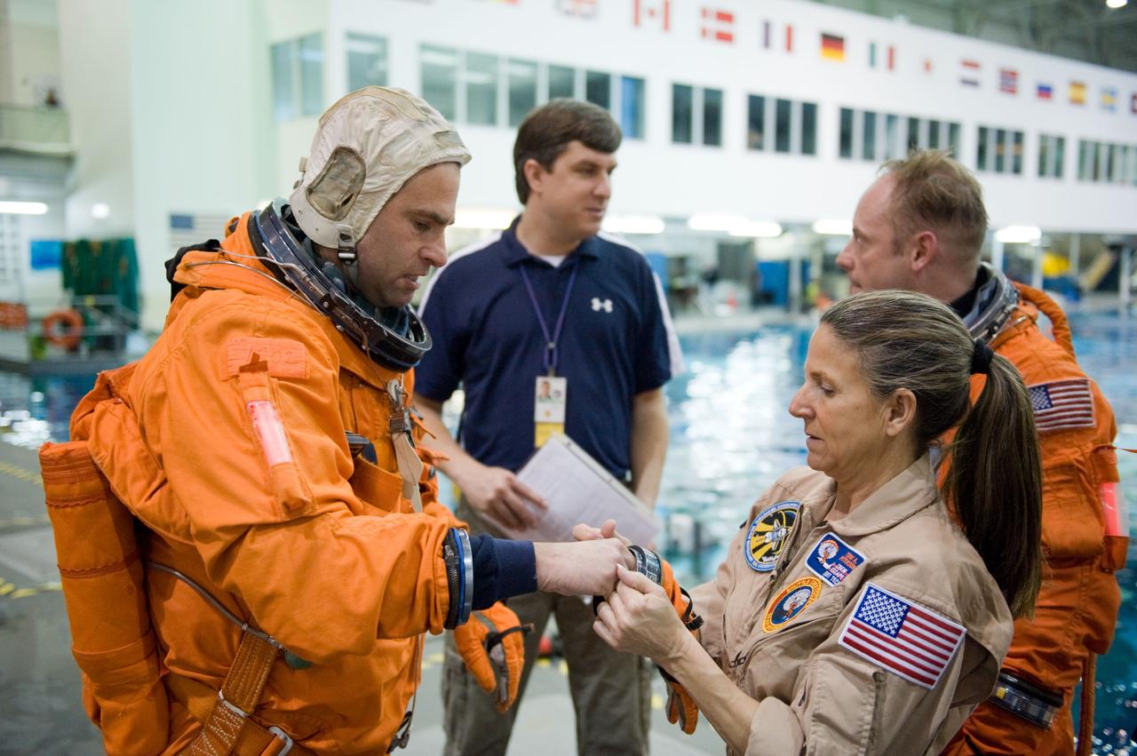 JSC2010-E-025726 (23 Feb. 2010) --- NASA astronaut Greg Chamitoff, STS-134 mission specialist, dons a training version of his shuttle launch and entry suit in preparation for a water survival training session in the Neutral Buoyancy Laboratory (NBL) near NASA's Johnson Space Center. United Space Alliance suit technician Toni Cost-Davis assisted Chamitoff. Astronaut Michael Fincke, mission specialist, is visible at right background.