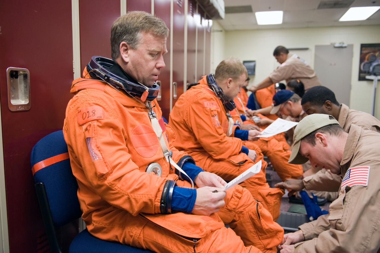 JSC2010-E-042073 (23 March 2010) --- NASA astronaut Steve Lindsey, STS-133 commander, reads a checklist as he gets help with the donning of a training version of his shuttle launch and entry suit in preparation for a training session in the Space Vehicle Mock-up Facility at NASA's Johnson Space Center. Astronaut Eric Boe, pilot, is visible in the background.
