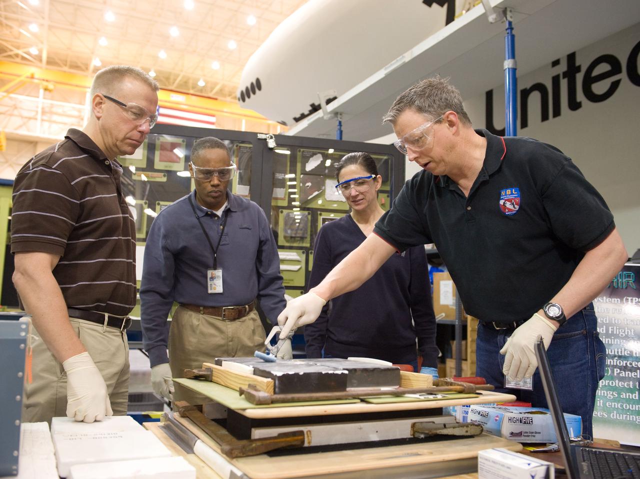 JSC2010-E-044335 (30 March 2010) --- NASA astronauts Tim Kopra (left), Nicole Stott and Alvin Drew, all STS-133 mission specialists, participate in an EVA tile repair training session in the Space Vehicle Mockup Facility at NASA's Johnson Space Center. Instructor John Ray (right) assisted the crew members.