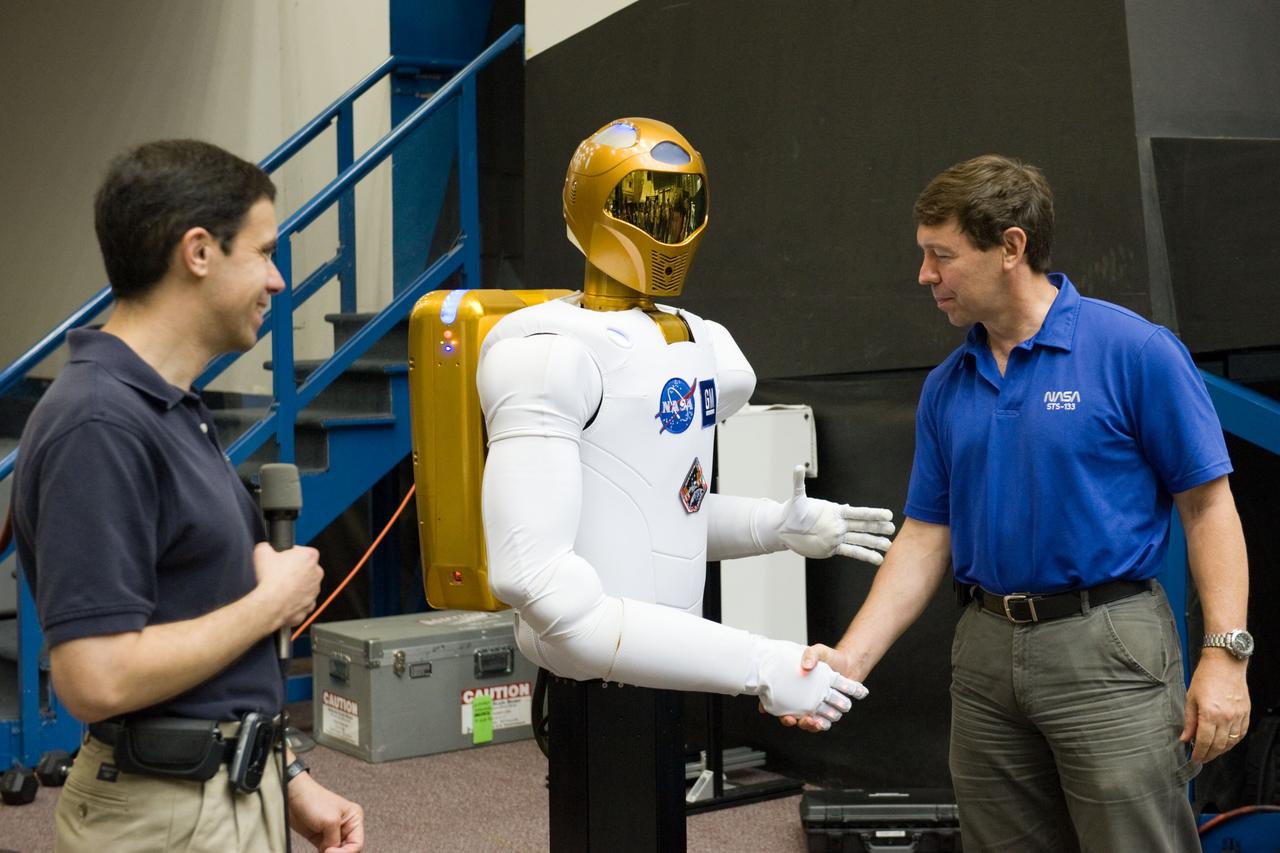 JSC2010-E-112701 (4 Aug. 2010) --- NASA astronaut Michael Barratt, STS-133 mission specialist, shakes hands with Robonaut 2 (R2) during media day in the Space Vehicle Mock-up Facility at NASA's Johnson Space Center. R2 is the first humanoid robot to travel to space and the first U.S.-built robot to visit the International Space Station. R2 will stay on the space station indefinitely to allow engineers on the ground to learn more about how humanoid robots fare in microgravity. Ron Diftler, NASA Robonaut project manager, is at left. Photo credit: NASA or National Aeronautics and Space Administration