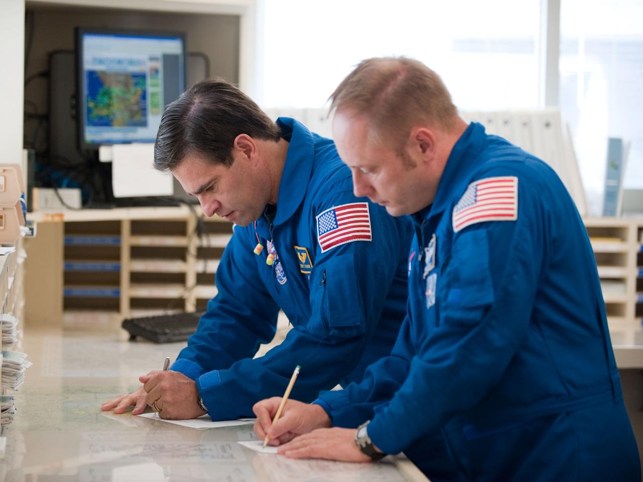 JSC2010-E-119526 (25 Aug. 2010) --- NASA astronauts Greg Chamitoff (background) and Michael Fincke, both STS-134 mission specialists, look over their flight plans in the check-out facility at Ellington Field near NASA's Johnson Space Center prior to a familiarization flight in NASA T-38 trainer jets. Photo credit: NASA or National Aeronautics and Space Administration