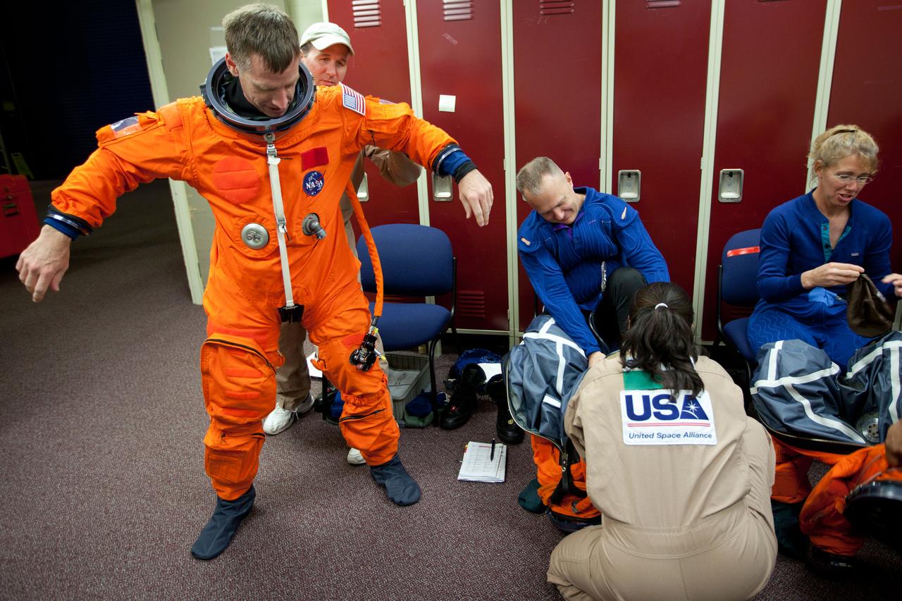 JSC2011-E-040270 (24 March 2011) --- NASA astronaut Chris Ferguson, left, STS-135 commander, dons his training version of a shuttle launch and entry suit before participating in a post-insertion training session with NASA astronauts Doug Hurley, pilot, and Sandy Magnus, mission specialist, March 24, 2011, in the Space Vehicle Mock-up Facility at NASA's Johnson Space Center in Houston. Hurley and Magnus are wearing their liquid-cooled undergarments for the orange suit. Photo credit: NASA Photo/Houston Chronicle, Smiley N. Pool