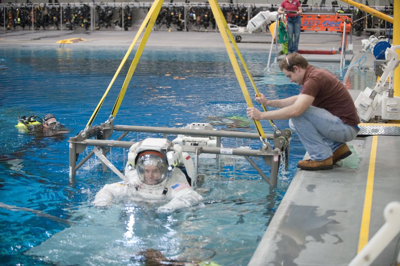 JSC2011-E-054089 (13 June 2011) --- NASA astronauts Rex Walheim and Sandy Magnus (mostly obscured), both STS-135 mission specialists, attired in training versions of their Extravehicular Mobility Unit (EMU) spacesuits, are raised from the waters of the Neutral Buoyancy Laboratory (NBL) near NASA's Johnson Space Center as a spacewalk training session comes to a close. Divers were in the water to assist Magnus and Walheim in their rehearsal. Photo credit: NASA
