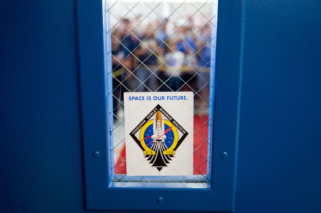 JSC2011-E-068761 (22 July 2011) --- A small portion of a large Ellington Field crowd is seen on July 22, 2011 through a door bearing a STS-135 sticker on its window. A short while later the crew of the space shuttle Atlantis' mission used this door for its entrance during a welcome home ceremony. STS-135 is the final mission of the NASA Space Shuttle Program. Photo credit: NASA Photo/Houston Chronicle, Smiley N. Pool