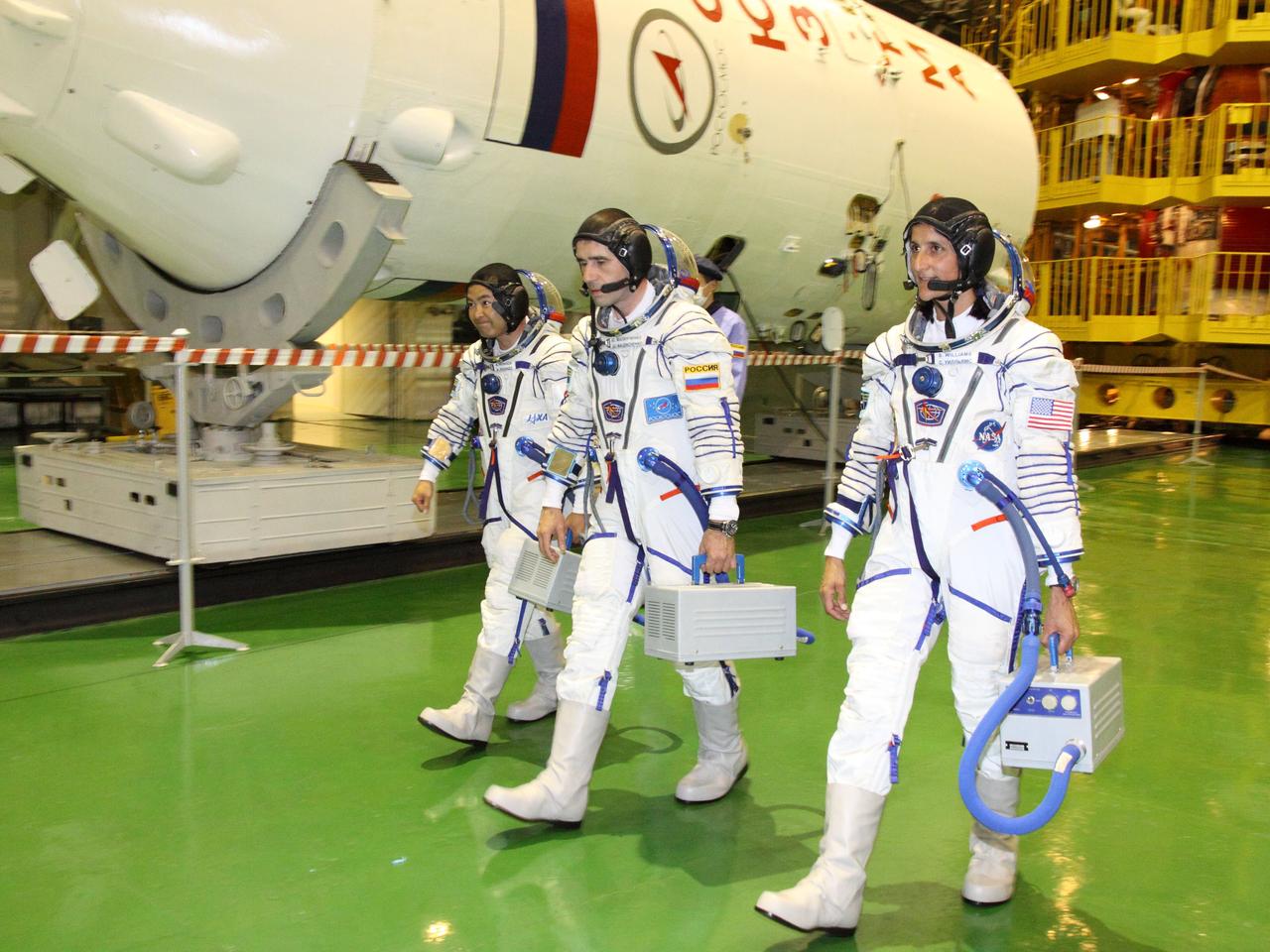 At the Baikonur Cosmodrome in Kazakhstan, Expedition 32/33 Flight Engineer Aki Hoshide of the Japan Aerospace Exploration Agency (left), Soyuz Commander Yuri Malenchenko (center) and NASA Flight Engineer Sunita Williams (right) walk by the upper stage of their Soyuz booster rocket in the Integration Facility July 3, 2012 as they completed a suited “fit check” of the Soyuz TMA-05M spacecraft that they will launch in July 15 to the International Space Station.  NASA/Victor Zelentsov 