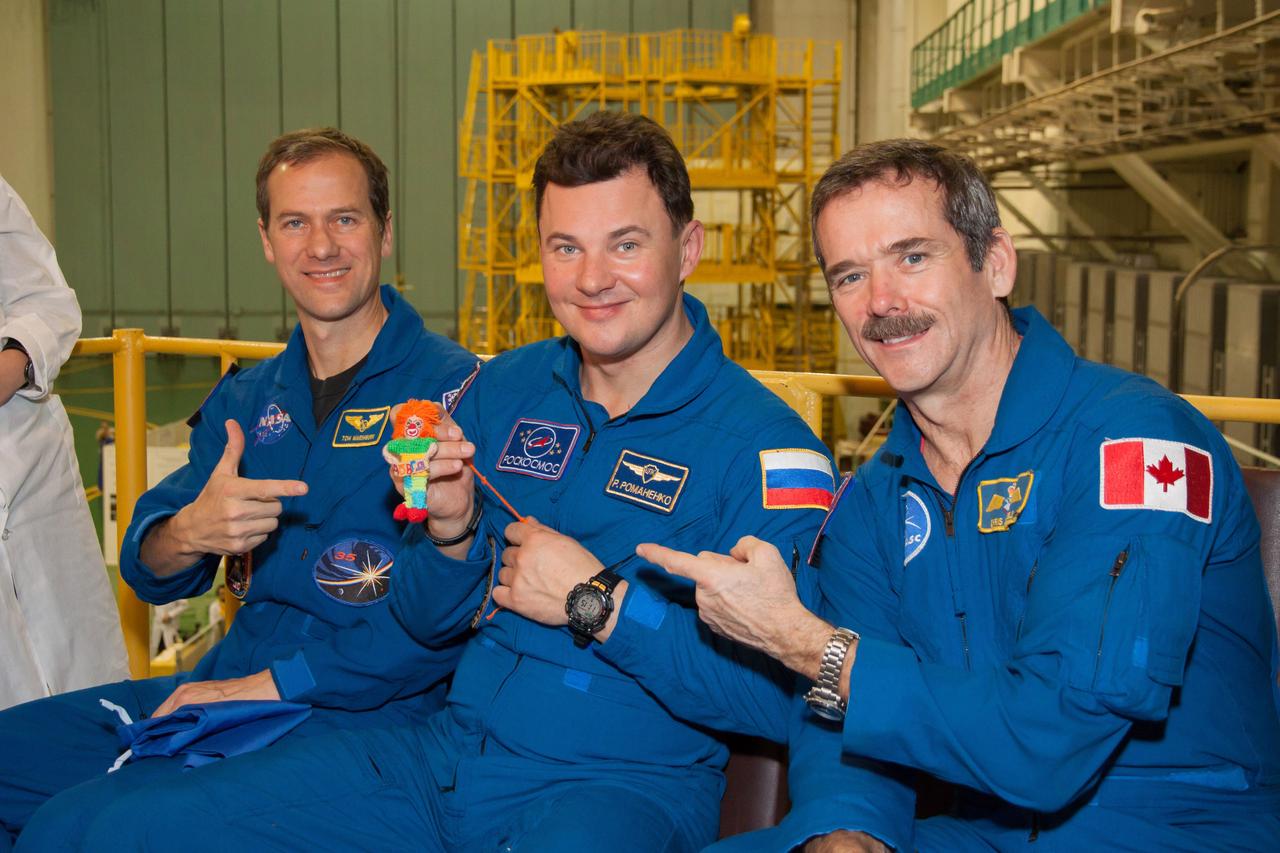 At the Baikonur Cosmodrome in Kazakhstan, Expedition 34/35 Soyuz Commander Roman Romanenko (center) holds a toy “talisman” that his 9-year old daughter, Anastasia, gave him to hang over his seat in the Soyuz TMA-07M spacecraft as a zero-G indicator during launch with his crewmates, Flight Engineer Tom Marshburn of NASA (left) and Flight Engineer Chris Hadfield of the Canadian Space Agency (right). The toy, named “Klyopa” for the Egyptian queen Cleopatra, was unveiled during a “fit check” dress rehearsal Dec. 7, 2012 in Baikonur leading to the crew’s launch Dec. 19 for a five-month mission on the International Space Station. Photo Credit: NASA/Victor Zelentsov