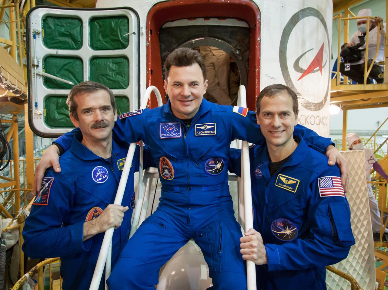 At the Integration Facility at the Baikonur Cosmodrome in Kazakhstan, Expedition 34/35 Flight Engineer Chris Hadfield of the Canadian Space Agency (left), Soyuz Commander Roman Romanenko (center) and Flight Engineer Tom Marshburn of NASA (right) pose for pictures in front of the Soyuz TMA-07M spacecraft Dec. 14, 2012 at the completion of the final “fit check” dress rehearsal for their launch Dec. 19 from Baikonur for a five-month mission on the International Space Station. NASA/Victor Zelentsov