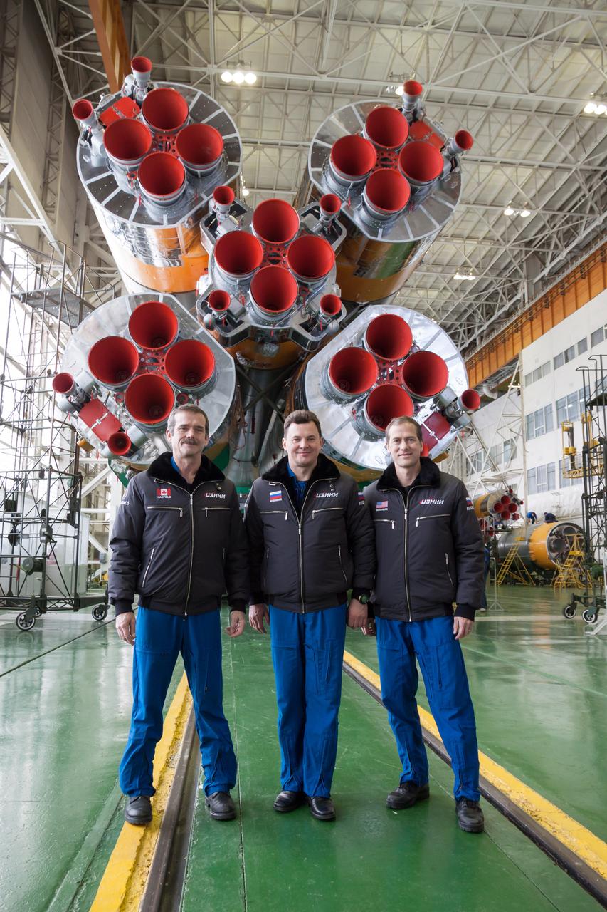 At the Integration Facility at the Baikonur Cosmodrome in Kazakhstan, Expedition 34/35 Flight Engineer Chris Hadfield of the Canadian Space Agency (left), Soyuz Commander Roman Romanenko (center) and Flight Engineer Tom Marshburn of NASA (right) pose for pictures in front of the cluster of first stage Soyuz booster engines Dec. 14, 2012 at the completion of the final “fit check” dress rehearsal for their launch Dec. 19 from Baikonur on the Soyuz TMA-07M spacecraft for a five-month mission on the International Space Station. NASA/Victor Zelentsov