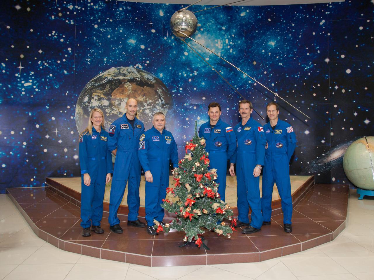 At the Korolev Museum at the Baikonur Cosmodrome in Kazakhstan, the Expedition 34/35 prime and backup crewmembers reflect the spirit of the holiday season as they pose for pictures in front of a wall mural depicting the cosmos and a model of Sputnik 1, the first satellite launched into orbit in October 1957 during ceremonial activities Dec. 14, 2012. From left to right are backup crewmembers Karen Nyberg of NASA, Luca Parmitano of the European Space Agency and Fyodor Yurchikhin and prime crewmembers Soyuz Commander Roman Romanenko, Flight Engineer Chris Hadfield of the Canadian Space Agency and Flight Engineer Tom Marshburn of NASA. Romanenko, Hadfield and Marshburn will launch Dec. 19 on the Soyuz TMA-07M spacecraft for a five-month mission on the International Space Station. NASA/Victor Zelentsov