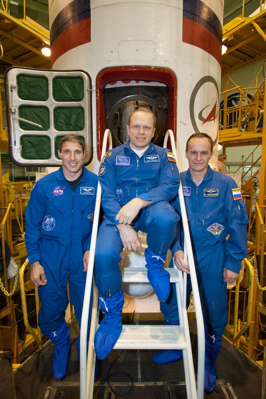 In the Integration Facility at the Baikonur Cosmodrome in Kazakhstan, Expedition 37/38 Flight Engineer Michael Hopkins of NASA (left), Soyuz Commander Oleg Kotov (center) and Flight Engineer Sergey Ryazanskiy (right) pose for pictures in front of their Soyuz TMA-10M spacecraft Sept. 20 as they completed a final “fit check” dress rehearsal of procedures leading to their launch Sept. 26, Kazakh time, from Baikonur to begin a five and a half month mission on the International Space Station.  NASA/Victor Zelentsov 
