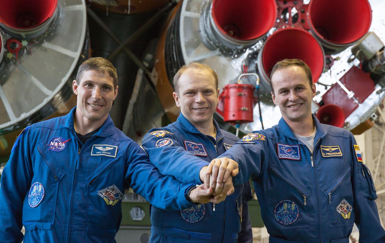 In the Integration Facility at the Baikonur Cosmodrome in Kazakhstan, Expedition 37/38 Flight Engineer Michael Hopkins of NASA (left), Soyuz Commander Oleg Kotov (center) and Flight Engineer Sergey Ryazanskiy (right) clasp hands in front of the first stage engines of the Soyuz booster rocket Sept. 20 as they completed a final “fit check” inspection of their Soyuz TMA-10M spacecraft. Hopkins, Kotov and Ryazanskiy are preparing for launch Sept. 26, Kazakh time, to begin a five and a half month mission on the International Space Station.  NASA/Victor Zelentsov 