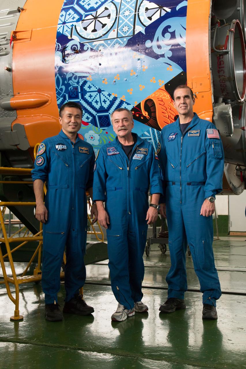 13-10-51-6:  In the Integration Facility at the Baikonur Cosmodrome in Kazakhstan, Expedition 38/39 Flight Engineer Koichi Wakata of the Japan Aerospace Exploration Agency (left), Soyuz Commander Mikhail Tyurin (center) and Flight Engineer Rick Mastracchio of NASA (right) pose for pictures Nov. 3 in front of the first stage of the Soyuz rocket during their final fit check dress rehearsal. The Soyuz rocket’s skirt is adorned with artwork representing the 2014 Winter Olympics in Sochi, Russia. The crewmembers, who will launch Nov. 7, Kazakh time for a six-month mission on the International Space Station, are carrying the Olympic torch to the complex with them for a four-day visit.  NASA/Victor Zelentsov 