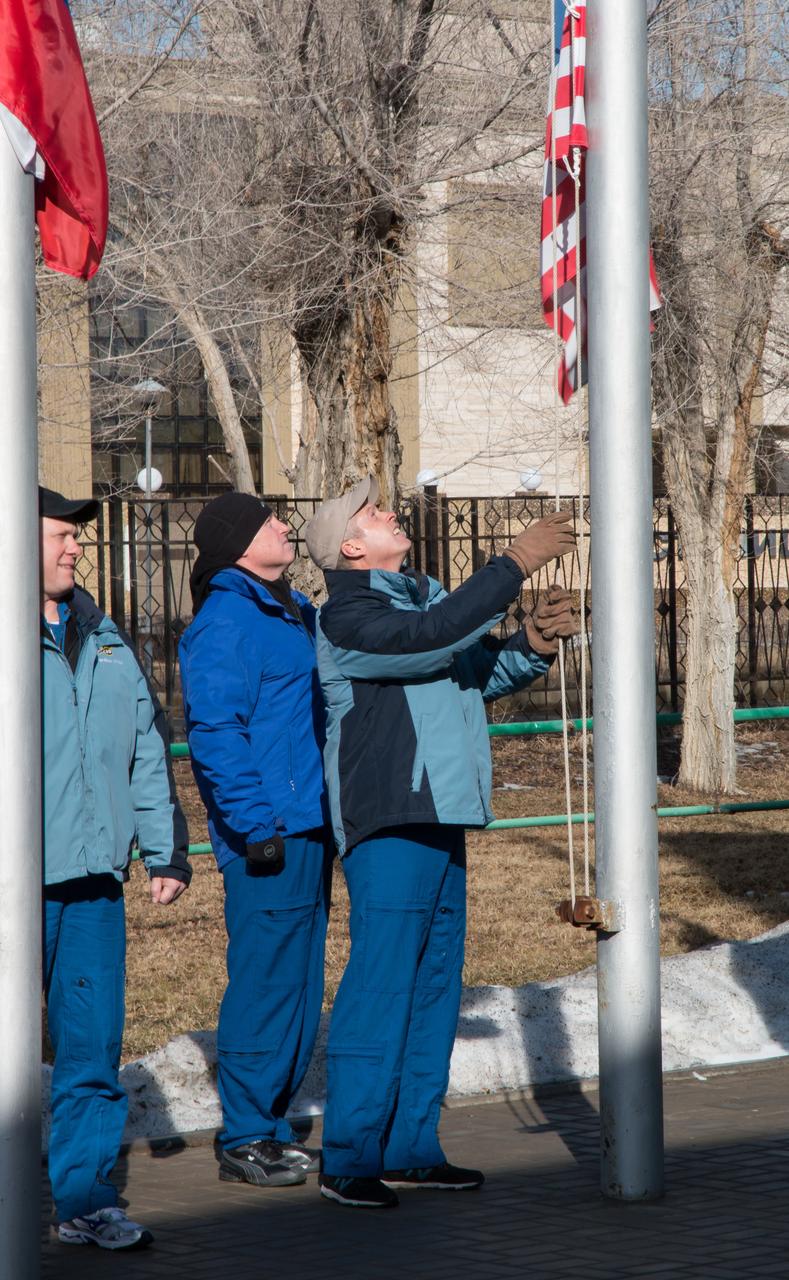 2014-03-15-11-03-42[1] At their Cosmonaut Hotel crew quarters in Baikonur, Kazakhstan, prime Expedition 39/40 Flight Engineer Steve Swanson of NASA (right) and backup Barry Wilmore of NASA (center) raise the American flag March 15 in traditional ceremonies that are part of the crew’s training. Prime crew Flight Engineer Oleg Artemyev (left) of the Russian Federal Space Agency (Roscosmos) looks on. Swanson, Artemyev and Soyuz Commander Alexander Skvortsov of Roscosmos are scheduled to launch to the International Space Station March 26 (Kazakh time) for the start of a six-month mission.  NASA/Victor Zelentsov 