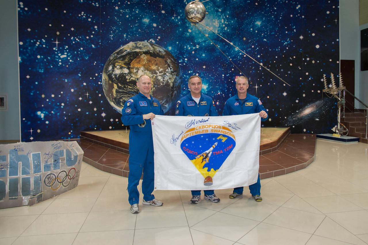 13-26-08: In the Baikonur Cosmodrome Museum in Kazakhstan, Expedition 39/40 Flight Engineer Oleg Artemyev of the Russian Federal Space Agency (Roscosmos; left), Soyuz Commander Alexander Skvortsov of Roscosmos (center) and Flight Engineer Steve Swanson of NASA (right) hold a banner bearing the insignia of their Soyuz crew patch March 21 during traditional ceremonies. Swanson, Skvortsov and Artemyev are wrapping up training for their launch to the station March 26, Kazakh time, Swanson, Skvortsov and Artemyev are wrapping up training for their launch to the station March 26, Kazakh time, on the Soyuz TMA-12 spacecraft for a six-month mission on the orbital laboratory. NASA/Victor Zelentsov