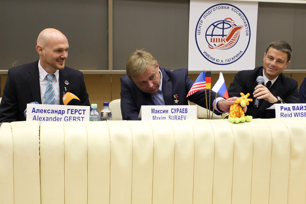 0687:  At the Gagarin Cosmonaut Training Center in Star City, Russia, Expedition 40/41 Soyuz Commander Max Suraev of the Russian Federal Space Agency (Roscosmos, center) plays with a toy giraffe at the crew’s pre-launch news conference May 8 while his crewmates, Alexander Gerst of the European Space Agency (left) and Reid Wiseman of NASA (right) look on. The giraffe, which belongs to Wiseman’s daughter, will fly as a “zero-G” mascot above the heads of the crew in the Soyuz TMA-13M spacecraft when they launch May 29, Kazakh time, from the Baikonur Cosmodrome in Kazakhstan for a 5 ½ month mission on the International Space Station.  NASA/Stephanie Stoll 