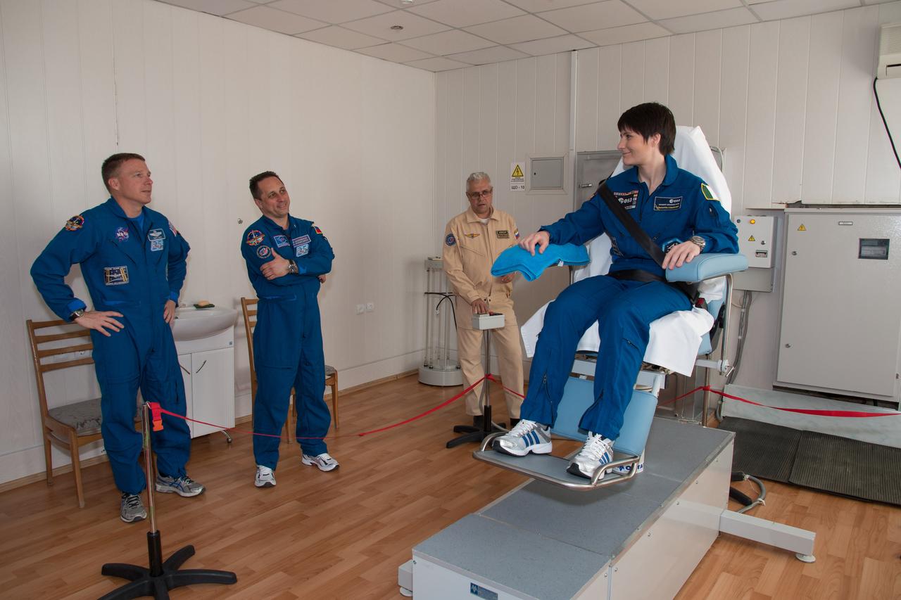 11-59-33-2:  At the Cosmonaut Hotel crew quarters in Baikonur, Kazakhstan, Expedition 40/41 backup crewmember Samantha Cristoforetti of the European Space Agency (right) prepares to take a ride in a spinning chair May 21 to exercise her vestibular system during pre-launch medical tests. Looking on are backup crewmates Terry Virts of NASA (far left) and Anton Shkaplerov of the Russian Federal Space Agency (Roscosmos, second from the left). The trio is backing up the prime crew, Flight Engineer Alexander Gerst of the European Space Agency, Soyuz Commander Max Suraev of Roscosmos and NASA Flight Engineer Reid Wiseman, who will launch on May 29, Kazakh time, on the Soyuz TMA-13M spacecraft from the Baikonur Cosmodrome for a 5 ½ month mission on the International Space Station.  NASA/Victor Zelentsov 