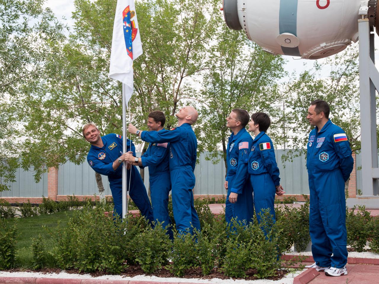 14-17-58:  Outside the Korolev Museum at the Baikonur Cosmodrome in Kazakhstan, Expedition 40/41 prime crewmembers Max Suraev of the Russian Federal Space Agency (Roscosmos, far left), Flight Engineer Reid Wiseman of NASA (second from left) and Alexander Gerst of the European Space Agency (third from left) raise the flag of their Soyuz crew insignia May 24 during traditional pre-launch ceremonies. Looking on are backup crewmembers Terry Virts of NASA (third from right), Samantha Cristoforetti of the European Space Agency (second from right) and Anton Shkaplerov (far right). Wiseman, Gerst and Suraev will launch May 29, Kazakh time, on the Soyuz TMA-13M spacecraft for a 5 ½ month mission on the International Space Station.  NASA/Victor Zelentsov 