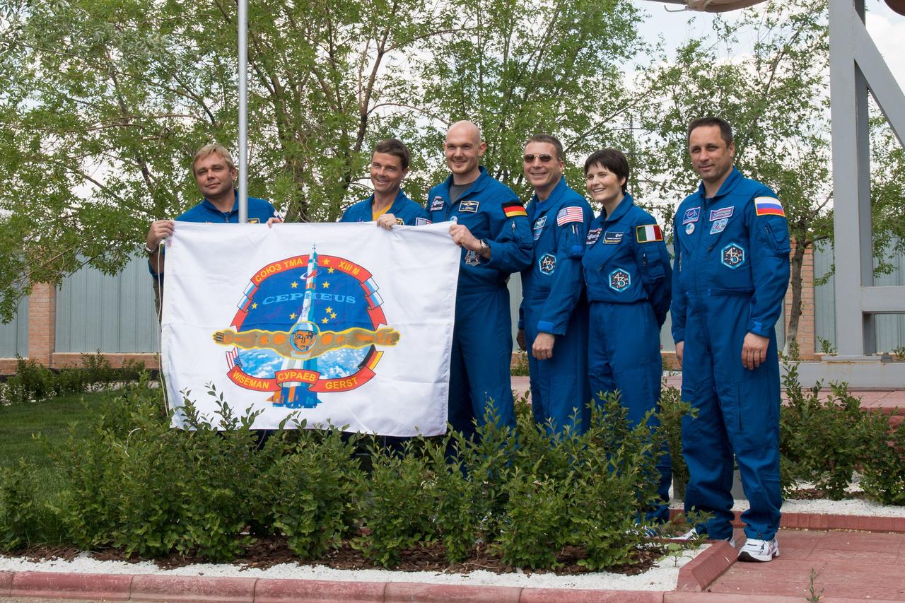 14-18-32:  Outside the Korolev Museum at the Baikonur Cosmodrome in Kazakhstan, Expedition 40/41 prime crewmembers Max Suraev of the Russian Federal Space Agency (Roscosmos, far left), Flight Engineer Reid Wiseman of NASA (second from left) and Alexander Gerst of the European Space Agency (third from left) display the flag of their Soyuz crew insignia May 24 during traditional pre-launch ceremonies. With them are backup crewmembers Terry Virts of NASA (third from right), Samantha Cristoforetti of the European Space Agency (second from right) and Anton Shkaplerov (far right). Wiseman, Gerst and Suraev will launch May 29, Kazakh time, on the Soyuz TMA-13M spacecraft for a 5 ½ month mission on the International Space Station.  NASA/Victor Zelentsov 