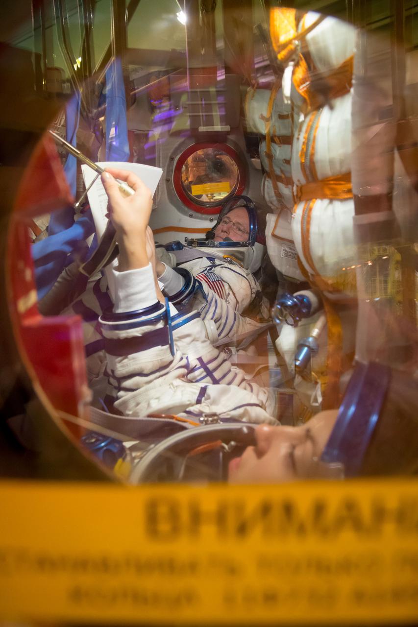 13-13-48-36-2: (13 Sept. 2014) --- At the Baikonur Cosmodrome in Kazakhstan, Expedition 41/42 Flight Engineer Barry Wilmore of NASA (background) participates in practice procedures in the Soyuz TMA-14M spacecraft Sept. 13 with his crewmates during the first of two “fit check” dress rehearsal activities. Flight Engineer Elena Serova of the Russian Federal Space Agency (Roscosmos) is seen in the foreground running through a test of Soyuz systems. Wilmore, Serova and Soyuz Commander Alexander Samokutyaev of Roscosmos (hidden from view) will launch on Sept. 26, Kazakh time, in the Soyuz to begin a 5 ½ month mission on the International Space Station. Serova will become the fourth Russian woman to fly in space. Photo credit: NASA/Victor Zelentsov