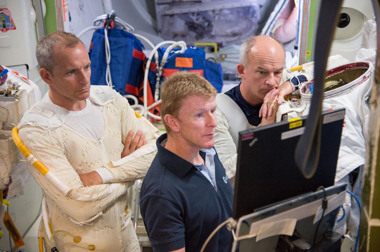 Expedition 47 ESA crewmember Tim Peake aiding fellow astronauts Expedition 48 crew member (Soyuz 46) Jeff Williams and CSA astronaut David Saint-Jacques during ISS EVA P/P training in Space Vehicle Mockup Training Facility (SVMTF) ISS Airlock mockup with instructor Megan Murphey. Photo Date: September 23, 2014. Location: Building 9NW, ISS Airlock. Photographer: Robert Markowitz