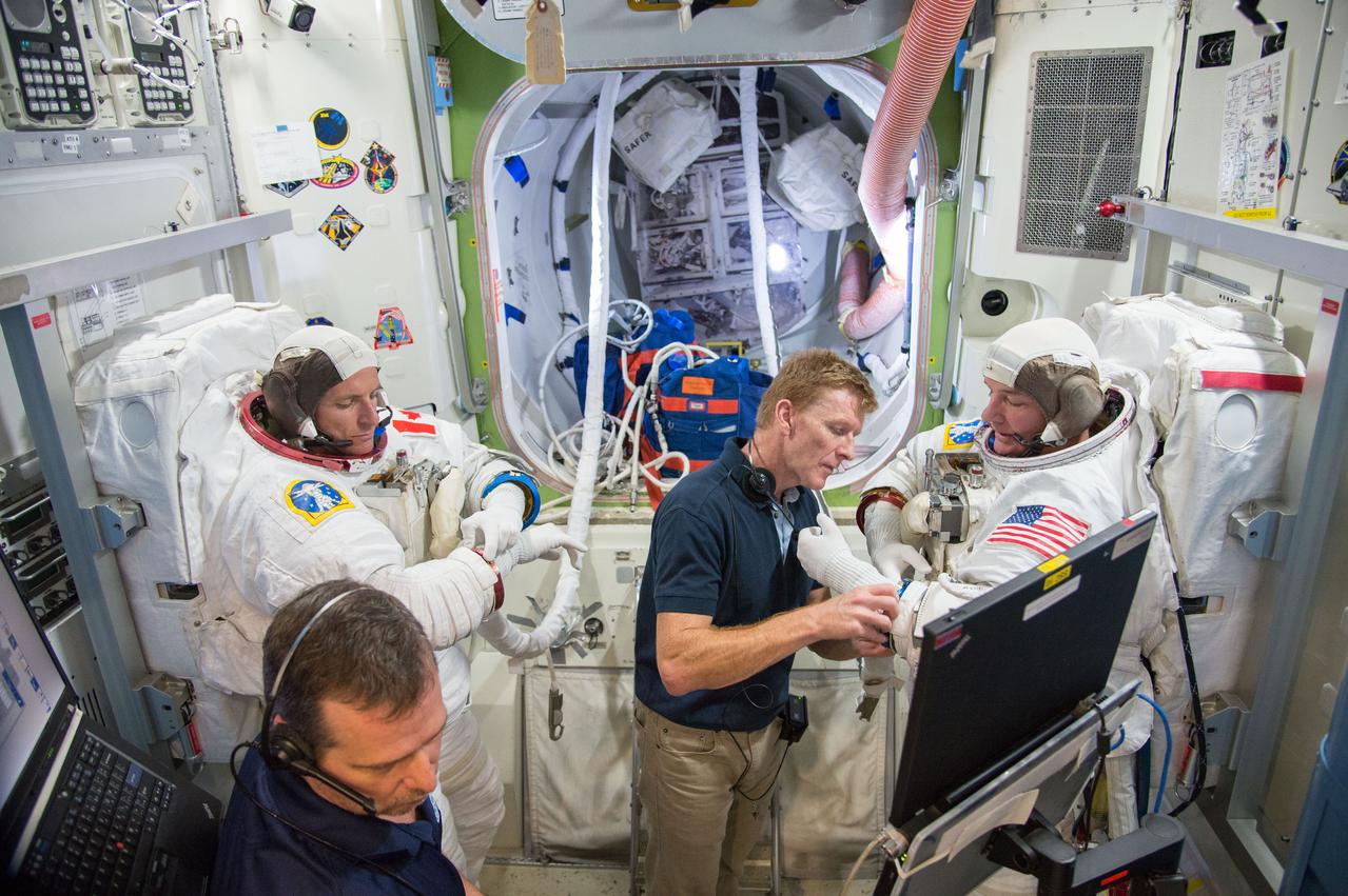 Expedition 47 ESA crewmember Tim Peake aiding fellow astronauts Expedition 48 crew member (Soyuz 46) Jeff Williams and CSA astronaut David Saint-Jacques during ISS EVA P/P training in Space Vehicle Mockup Training Facility (SVMTF) ISS Airlock mockup with instructor Megan Murphey. Photo Date: September 23, 2014. Location: Building 9NW, ISS Airlock. Photographer: Robert Markowitz