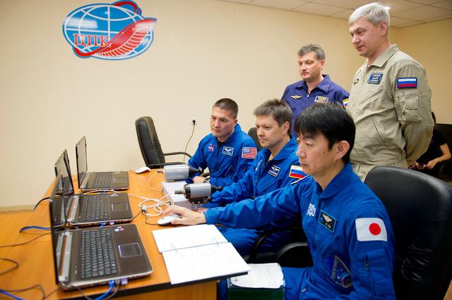 NASA image: 3918:..At the Cosmonaut Hotel crew quarters in Baikonur, Kazakhstan, Expedition 44 crewmembers Kjell Lindgren of NASA (left), Oleg Kononenko of the Russian Federal Space Agency (center) and Kimiya Yui of the Japan Aerospace Exploration Agency (right) rehearse rendezvous and docking techniques on a laptop computer as their trainers look on July 15. Yui, Kononenko and Lindgren will launch July 23, Kazakh time on the Soyuz TMA-17M spacecraft from the Baikonur Cosmodrome for a five-month mission on the International Space Station..