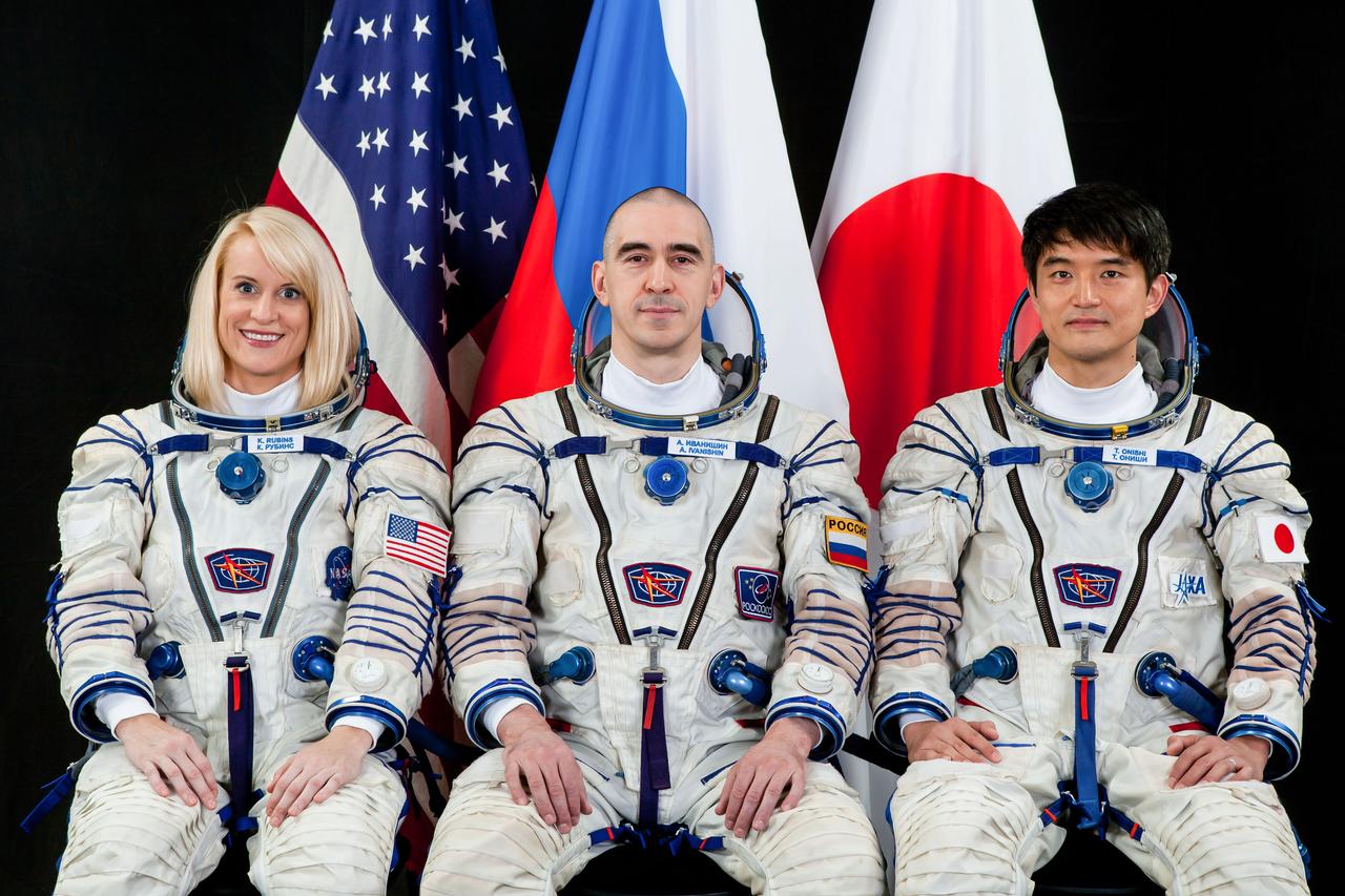 JSC2015e102000 (08/04/2015) --- Portrait of Expedition 48/49 crewmembers. From the left: NASA astronaut Kate Rubins, Russian cosmonaut Anatoly Ivanishin (Expedition 49 Commander) and Japan Aerospace Exploration Agency (JAXA) astronaut Takuya Onishi. All are wearing Russian Sokol launch and entry suits with the flags of the United States, Russia and Japan visible in the background.