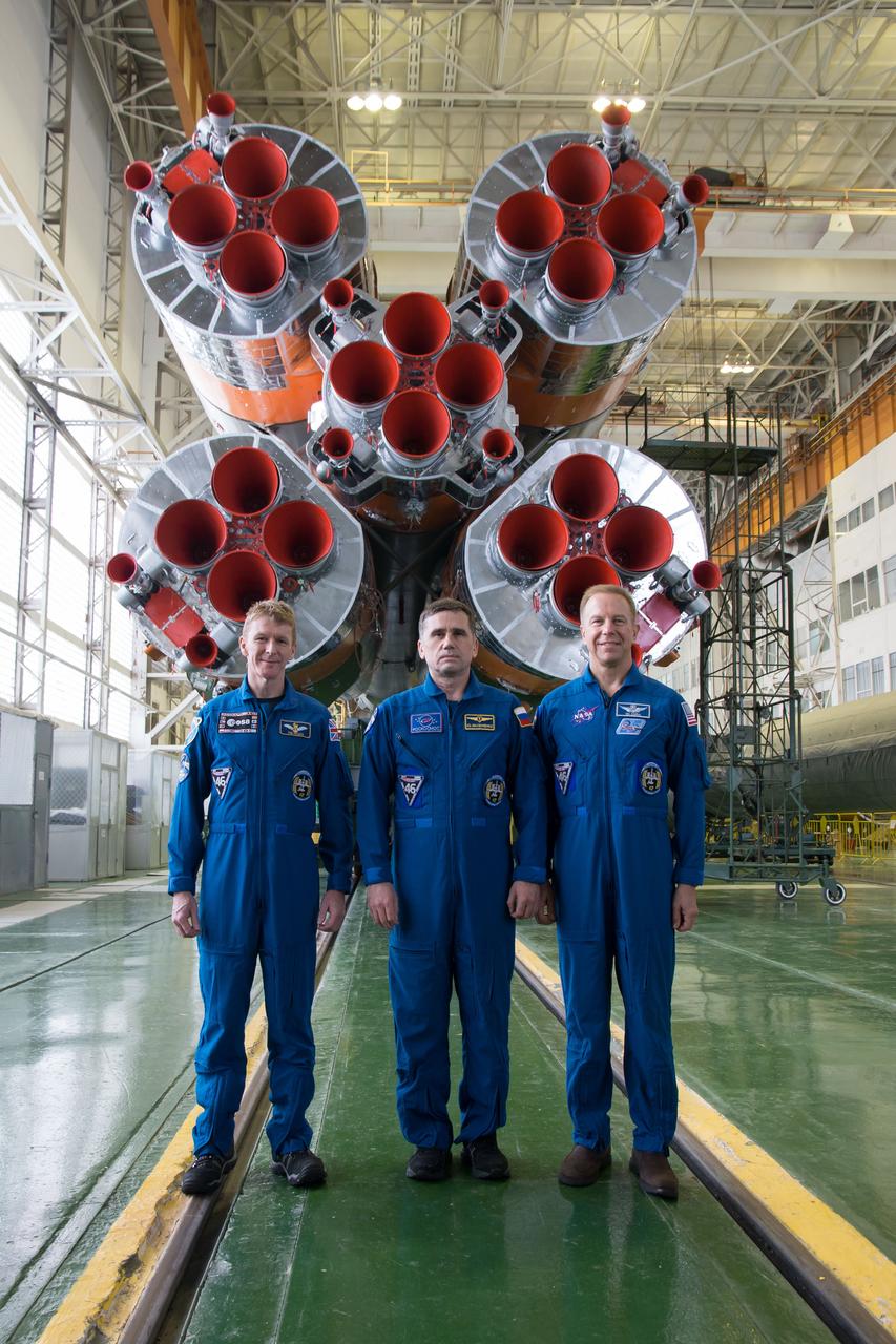 In the Integration Facility at the Baikonur Cosmodrome in Kazakhstan, Expedition 46-47 crewmembers Tim Peake of the European Space Agency (left), Yuri Malenchenko of the Russian Federal Space Agency (Roscosmos, center) and Tim Kopra of NASA (right) posed for pictures Dec. 10 in front of the first stage of the Soyuz booster rocket during final pre-launch training. Kopra, Peake and Malenchenko will launch Dec. 15 on the Soyuz TMA-19M spacecraft for a six-month mission on the International Space Station.  NASA/Victor Zelentsov 