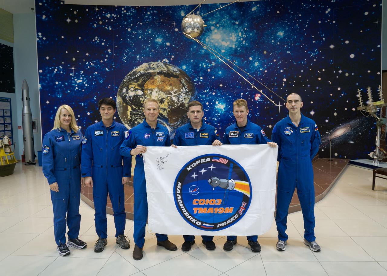 During a break from training, the Expedition 46-47 prime and backup crewmembers toured the Korolev Museum at the Baikonur Cosmodrome in Kazakhstan Dec. 10 and displayed a flag bearing the logo for the prime crew’s Soyuz mission. From left to right are backup crewmembers Kate Rubins of NASA and Takuya Onishi of the Japan Aerospace Exploration Agency, prime crewmembers Tim Kopra of NASA, Yuri Malenchenko of the Russian Federal Space Agency (Roscosmos) and Tim Peake of the European Space Agency who are holding the flag, and backup crewmember Anatoly Ivanishin of Roscosmos. Kopra, Peake and Malenchenko will launch Dec. 15 on the Soyuz TMA-19M spacecraft for a six-month mission on the International Space Station. NASA/Victor Zelentsov