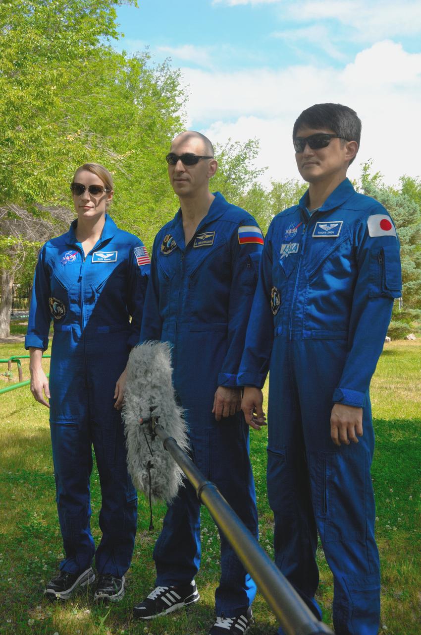 Outside their Cosmonaut Hotel crew quarters in Baikonur, Kazakhstan, Kate Rubins of NASA (left), Anatoly Ivanishin of Roscosmos (center) and Takuya Onishi of the Japan Aerospace Exploration Agency (right) answer reporters’ questions June 26 as they continue preparations for launch on July 7, Baikonur time, on the Soyuz MS-01 spacecraft for a planned four-month mission on the International Space Station.  NASA/Alexander Vysotsky 