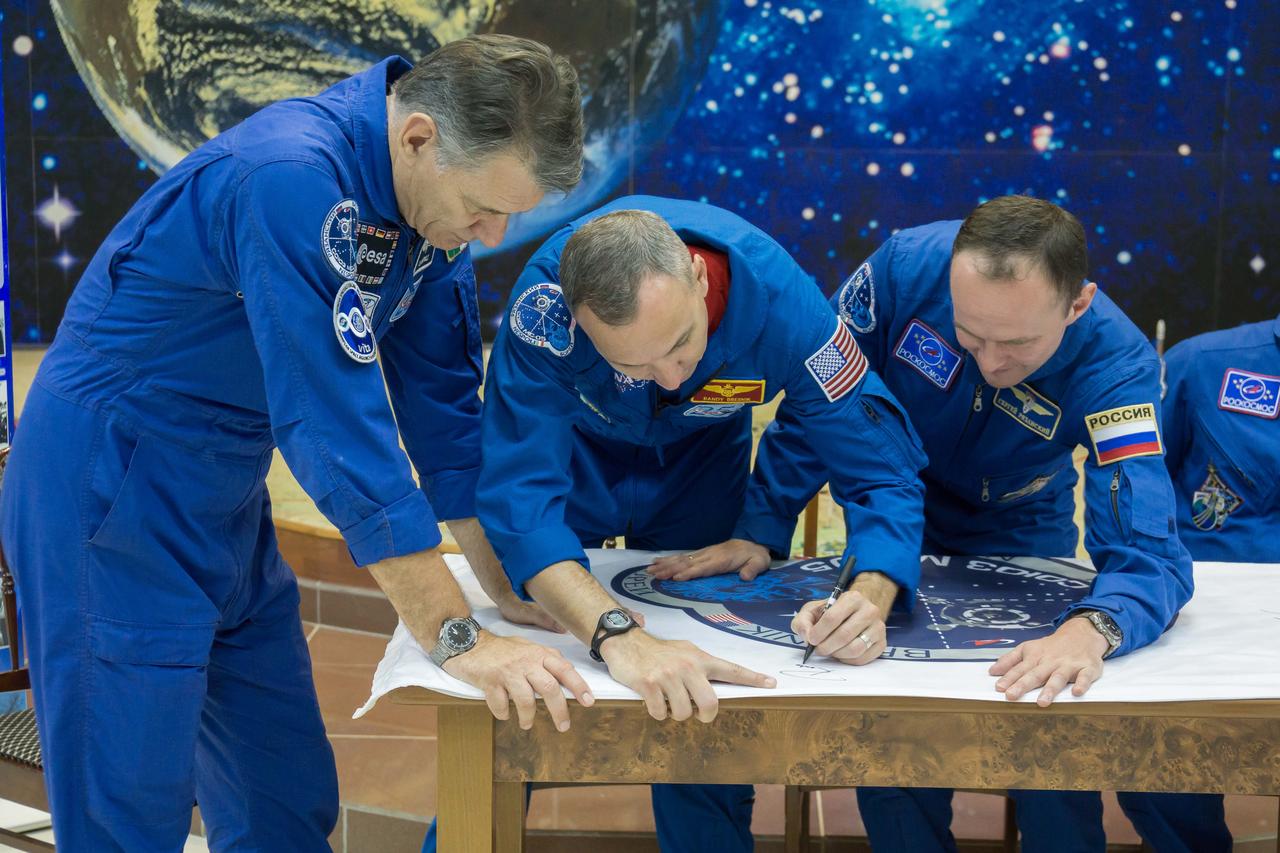 jsc2017e101948 (July 22, 2017) --- At the Baikonur Cosmodrome in Kazakhstan, Expedition 52-53 crewmembers Paolo Nespoli of the European Space Agency (left), Randy Bresnik of NASA (center) and Sergey Ryazanskiy of the Russian Federal Space Agency (Roscosmos, right) sign a flag bearing their Soyuz spacecraft insignia July 24 as part of traditional pre-launch activities. Nespoli, Bresnik and Ryazanskiy will launch July 28 aboard the Soyuz MS-05 spacecraft for a five-month mission on the International Space Station. Credit: NASA/Victor Zelentsov