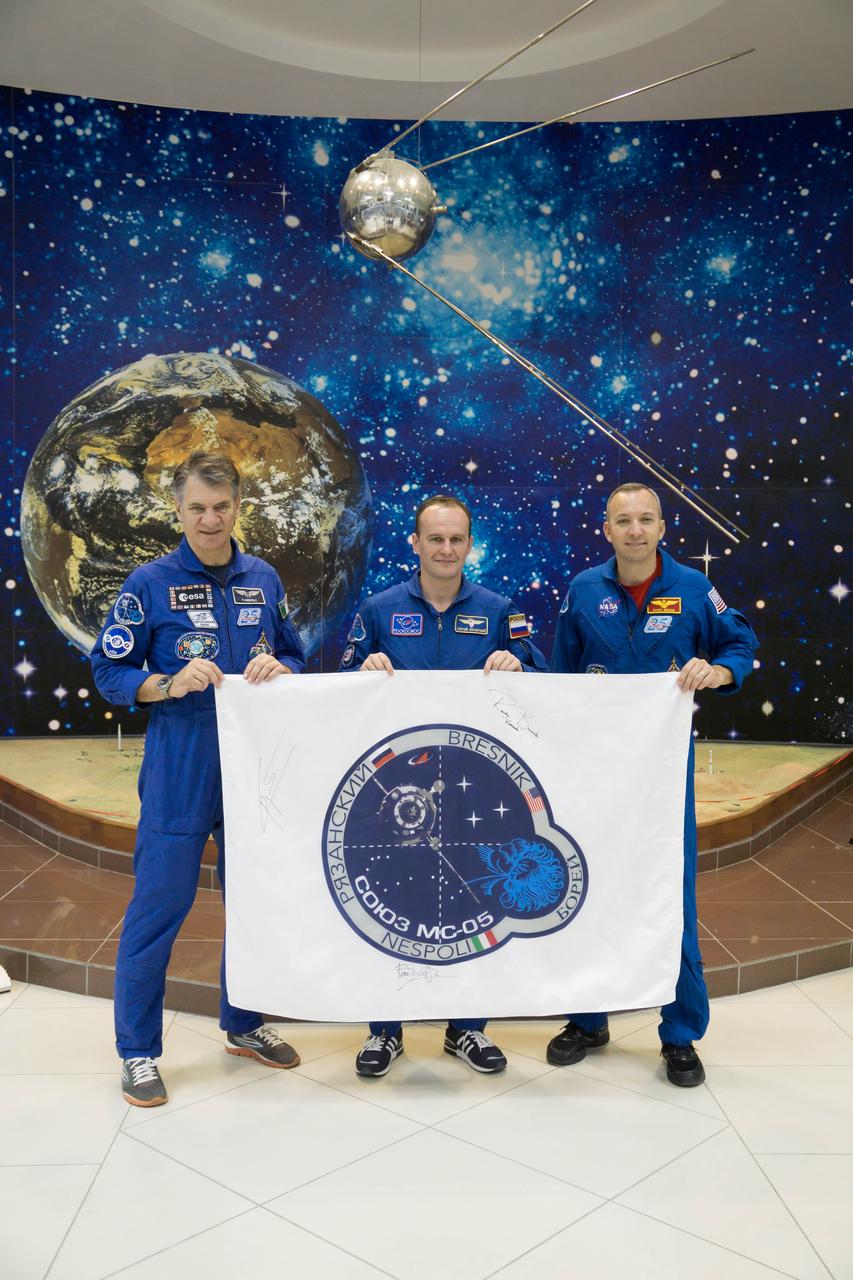 jsc2017e101950 (July 22, 2017) --- At the Baikonur Cosmodrome in Kazakhstan, Expedition 52-53 crewmembers Paolo Nespoli of the European Space Agency (left), Sergey Ryazanskiy of the Russian Federal Space Agency (Roscosmos, center) and Randy Bresnik (right) display a flag bearing their Soyuz spacecraft insignia at the Korolev Museum July 24 as part of traditional pre-launch activities. Nespoli, Bresnik and Ryazanskiy will launch July 28 aboard the Soyuz MS-05 spacecraft for a five-month mission on the International Space Station. Credit: NASA/Victor Zelentsov