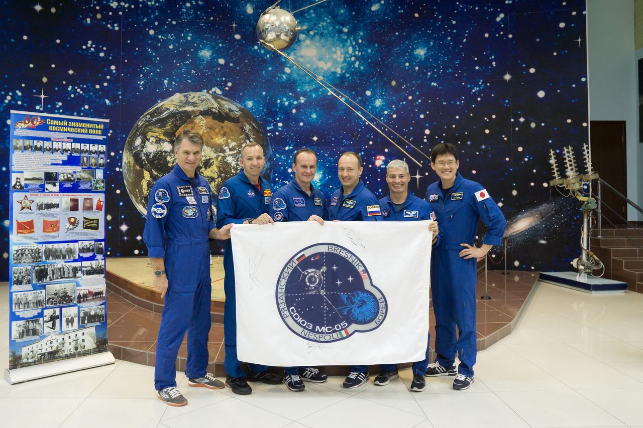 jsc2017e101951 (July 22, 2017) --- At the Baikonur Cosmodrome in Kazakhstan, the Expedition 52-53 prime and backup crewmembers pose for pictures with a flag bearing their Soyuz insignia at the Korolev Museum July 24 as part of traditional pre-launch activities. From left to right are prime crewmembers Paolo Nespoli of the European Space Agency, Randy Bresnik of NASA and Sergey Ryazanskiy of the Russian Federal Space Agency (Roscosmos) and backup crewmembers Alexander Misurkin of Roscosmos, Mark Vande Hei of NASA and Norishige Kanai of the Japan Aerospace Exploration Agency (JAXA). Nespoli, Bresnik and Ryazanskiy will launch July 28 aboard the Soyuz MS-05 spacecraft for a five-month mission on the International Space Station. Credit: NASA/Victor Zelentsov