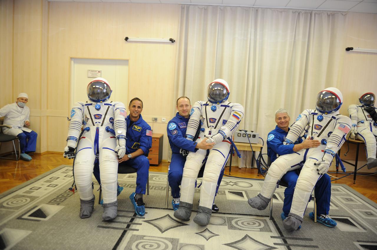 jsc2017e114477 (Aug. 28, 2017) --- In the Integration Facility at the Baikonur Cosmodrome in Kazakhstan, Expedition 53-54 crewmembers Joe Acaba of NASA (let), Alexander Misurkin of Roscosmos (center) and Mark Vande Hei of NASA (right) hold up their Sokol launch and entry suits for photographers Aug. 28 during pre-launch training activities. The trio will launch Sept. 13 on the Soyuz MS-06 spacecraft for a five and a half month mission on the International Space Station. Credit: Gagarin Cosmonaut Training Center/Irina Peshkova