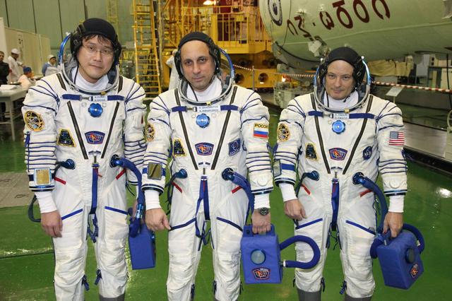 jsc2017e136441 - In the Integration Facility at the Baikonur Cosmodrome in Kazakhstan, Expedition 54-55 crewmembers Norishige Kanai of the Japan Aerospace Exploration Agency (JAXA, left),  Anton Shkaplerov of the Russian Federal Space Agency (Roscosmos, center) and Scott Tingle of NASA (right) pose for pictures Dec. 5 as part of their first fit check dress rehearsal activities. They will launch Dec. 17 in the Soyuz MS-07 vehicle for a five-month mission on the International Space Station...Courtesy of Roscosmos.