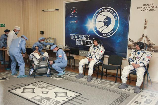 jsc2017e136442 - In the Integration Facility at the Baikonur Cosmodrome in Kazakhstan, Expedition 54-55 crewmember Anton Shkaplerov of the Russian Federal Space Agency (Roscosmos) undergoes a leak check on his Sokol launch and entry suit Dec. 5 as part of the first fit check dress rehearsal activities while crewmates Norishige Kanai of the Japan Aerospace Exploration Agency (JAXA, left) and Scott Tingle of NASA (right) look on. They will launch Dec. 17 in the Soyuz MS-07 vehicle for a five-month mission on the International Space Station...Courtesy of Roscosmos.