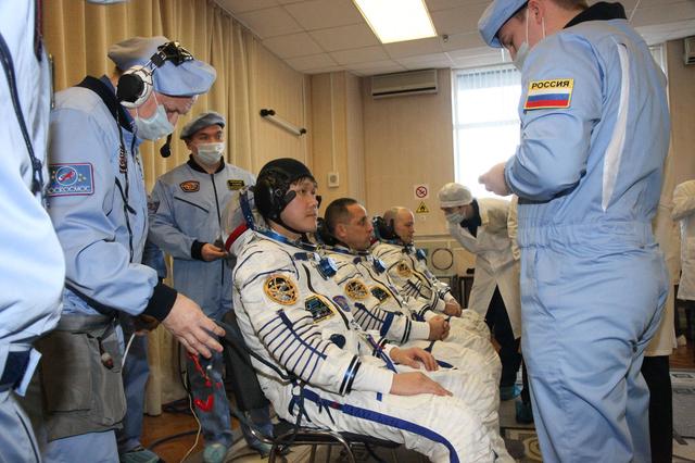 jsc2017e136444 - In the Integration Facility at the Baikonur Cosmodrome in Kazakhstan, Expedition 54-55 crewmembers Norishige Kanai of the Japan Aerospace Exploration Agency (JAXA, left), Anton Shkaplerov of the Russian Federal Space Agency (Roscosmos, center) and Scott Tingle of NASA (right) listen to a briefing by technicians Dec. 5 for the first fit check dress rehearsal activity in the Soyuz MS-07 spacecraft. They will launch Dec. 17 in the Soyuz MS-07 vehicle for a five-month mission on the International Space Station...Courtesy of Roscosmos.