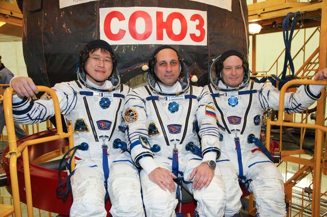 jsc2017e136445 - In the Integration Facility at the Baikonur Cosmodrome in Kazakhstan, Expedition 54-55 crewmembers Norishige Kanai of the Japan Aerospace Exploration Agency (JAXA, left), Anton Shkaplerov of the Russian Federal Space Agency (Roscosmos, center) and Scott Tingle of NASA (right) pose for pictures in front of their Soyuz MS-07 spacecraft Dec. 5 as part of their first fit check dress rehearsal activities. They will launch Dec. 17 in the Soyuz MS-07 vehicle for a five-month mission on the International Space Station...Courtesy of Roscosmos.