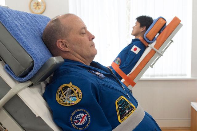jsc2017e137341 - At the Cosmonaut Hotel crew quarters in Baikonur, Kazakhstan, Expedition 54-55 prime crewmembers Scott Tingle of NASA (left) and Norishige Kanai of the Japan Aerospace Exploration Agency (right) test their vestibular skills on tilt tables Dec. 11 as part of their pre-launch training. Along with Anton Shkaplerov of the Russian Federal Space Agency (Roscosmos), they will launch Dec. 17 on the Soyuz MS-07 spacecraft from the Baikonur Cosmodrome for a five month mission on the International Space Station...Andrey Shelepin / Gagarin Cosmonaut Training Center.