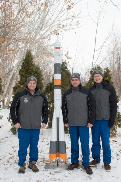 jsc2017e137343 - At their Cosmonaut Hotel crew quarters in Baikonur, Kazakhstan, Expedition 54-55 prime crewmembers Scott Tingle of NASA (left), Anton Shkaplerov of the Russian Federal Space Agency (Roscosmos, center) and Norishige Kanai of the Japan Aerospace Exploration Agency (JAXA, right) pose for pictures by a model of a Soyuz rocket Dec. 11. They will launch Dec. 17 on the Soyuz MS-07 spacecraft from the Baikonur Cosmodrome for a five month mission on the International Space Station...Andrey Shelepin / Gagarin Cosmonaut Training Center.