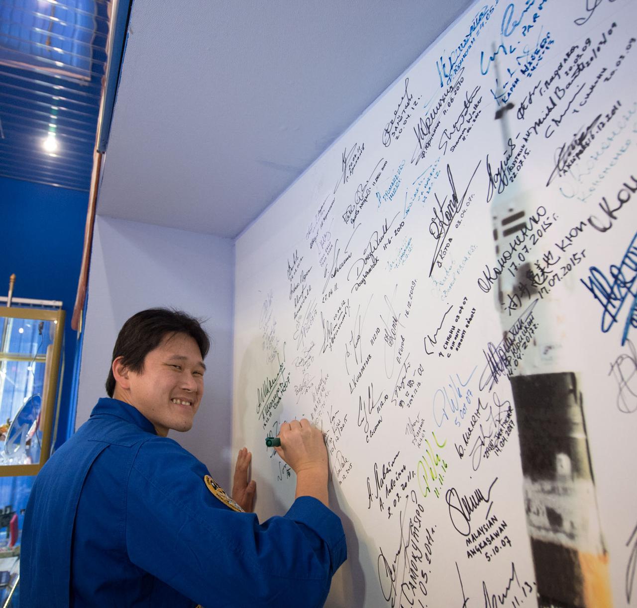 jsc2017e138116 - At the Korolev Museum at the Baikonur Cosmodrome in Kazakhstan, Expedition 54-55 prime crewmember Norishige Kanai of the Japan Aerospace Exploration Agency (JAXA) signs a wall mural Dec. 13 as part of traditional pre-launch ceremonies. Kanai, Scott Tingle of NASA and Anton Shkaplerov of the Russian Federal Space Agency (Roscosmos) will launch Dec. 17 on the Soyuz MS-07 spacecraft for a five month mission on the International Space Station...Andrey Shelepin/Gagarin Cosmonaut Training Center.