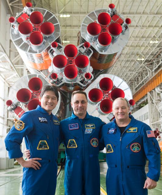 jsc2017e138119 - In the Integration Facility at the Baikonur Cosmodrome in Kazakhstan, the Expedition 54-55 prime crewmembers pose for pictures Dec. 13 in front of the first stage of the Soyuz booster rocket. From left to right are Norishige Kanai of the Japan Aerospace Exploration Agency (JAXA), Scott Tingle of NASA and Anton Shkaplerov of the Russian Federal Space Agency (Roscosmos), who will launch Dec. 17 on the Soyuz MS-07 spacecraft for a five month mission on the International Space Station...Andrey Shelepin/Gagarin Cosmonaut Training Center.